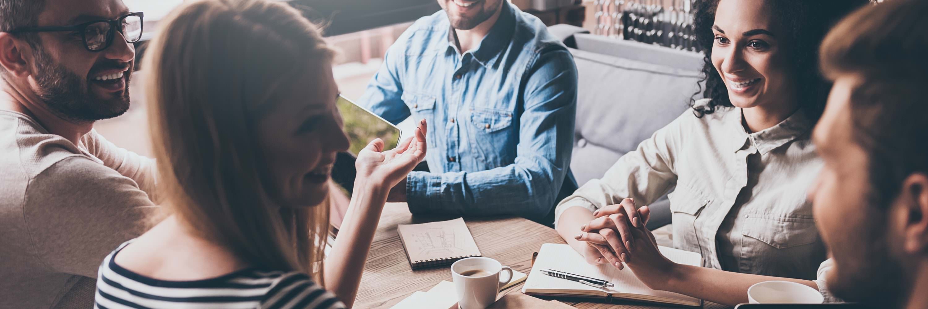 Cheerful young people looking at each other with smile while sitting at the office table at the business meeting